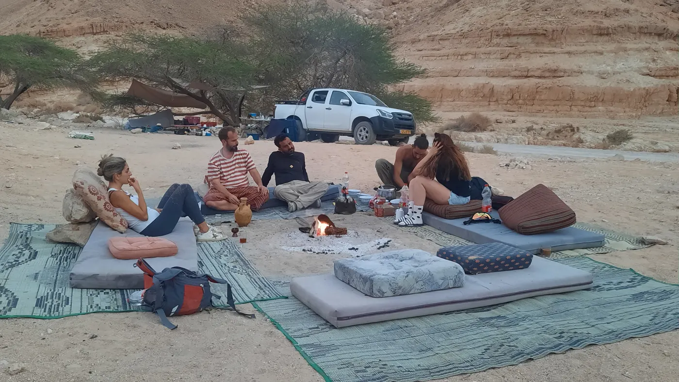 מחנה במדבר עם מזרונים ושטיחים סביב מדורה